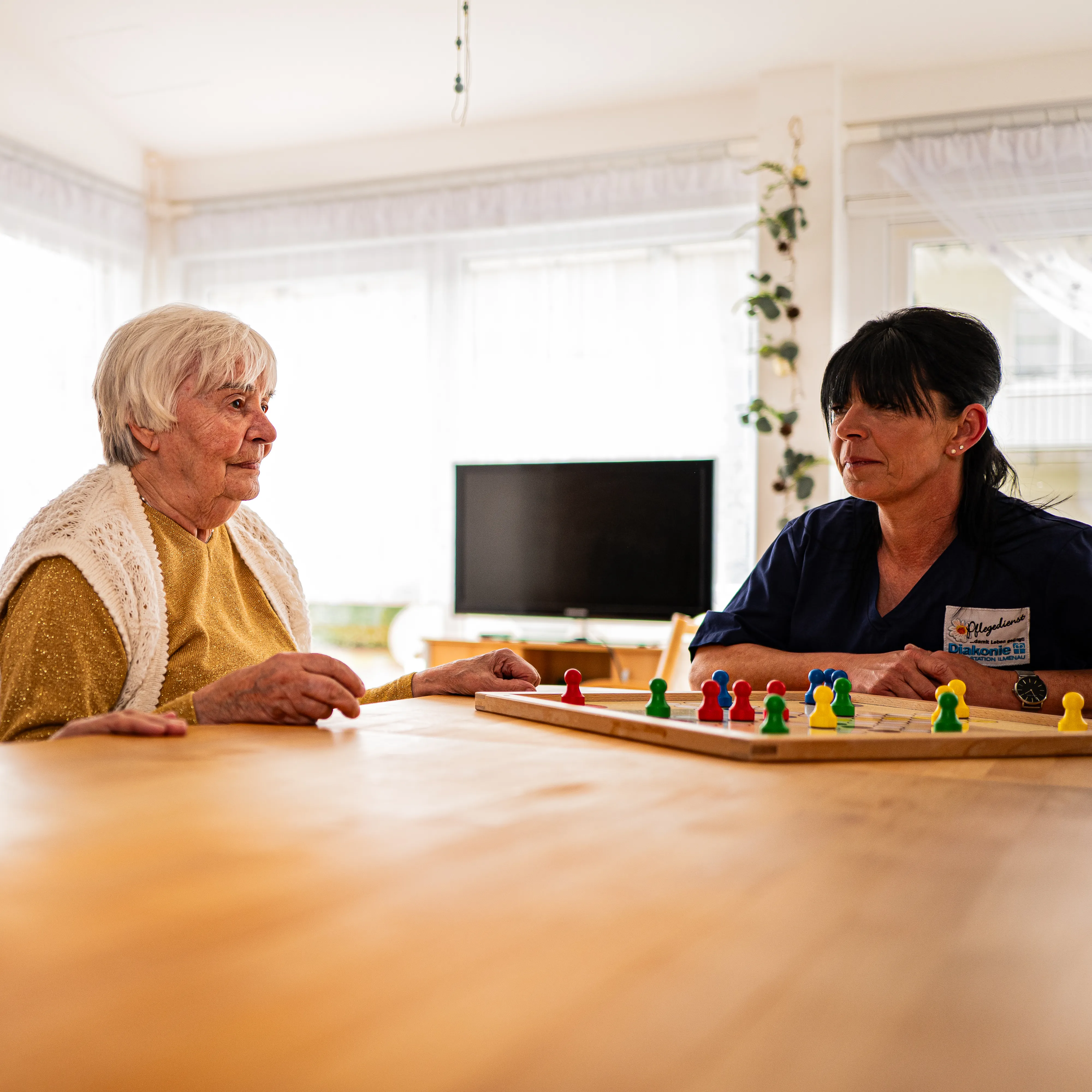 Pflegekraft und Seniorin spielen gemeinsam ein Brettspiel im Alltag
