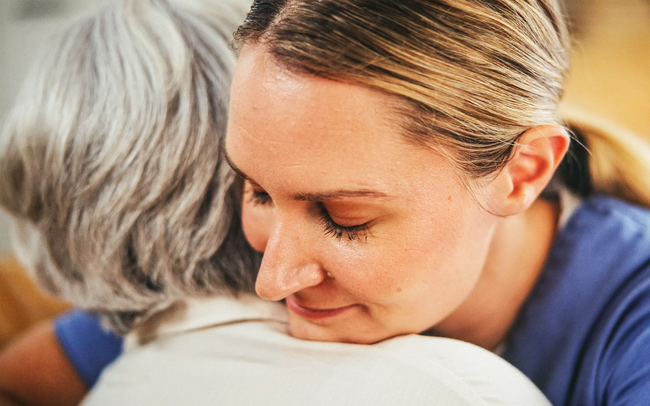 Pflegekraft umarmt Seniorin unterstützend im Alltag