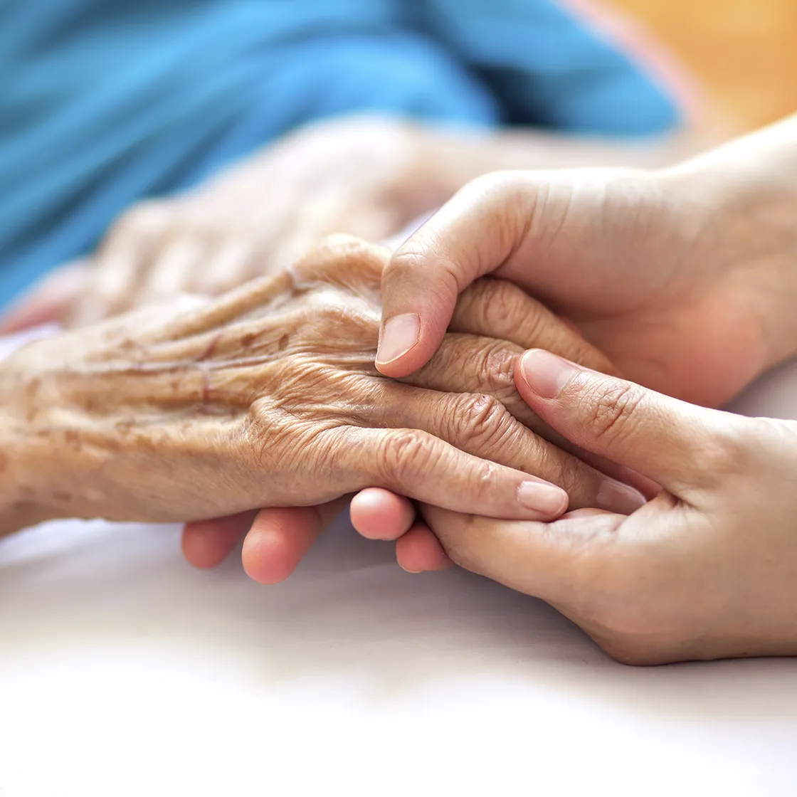 Hände einer Pflegekraft halten unterstützend die Hand einer Seniorin