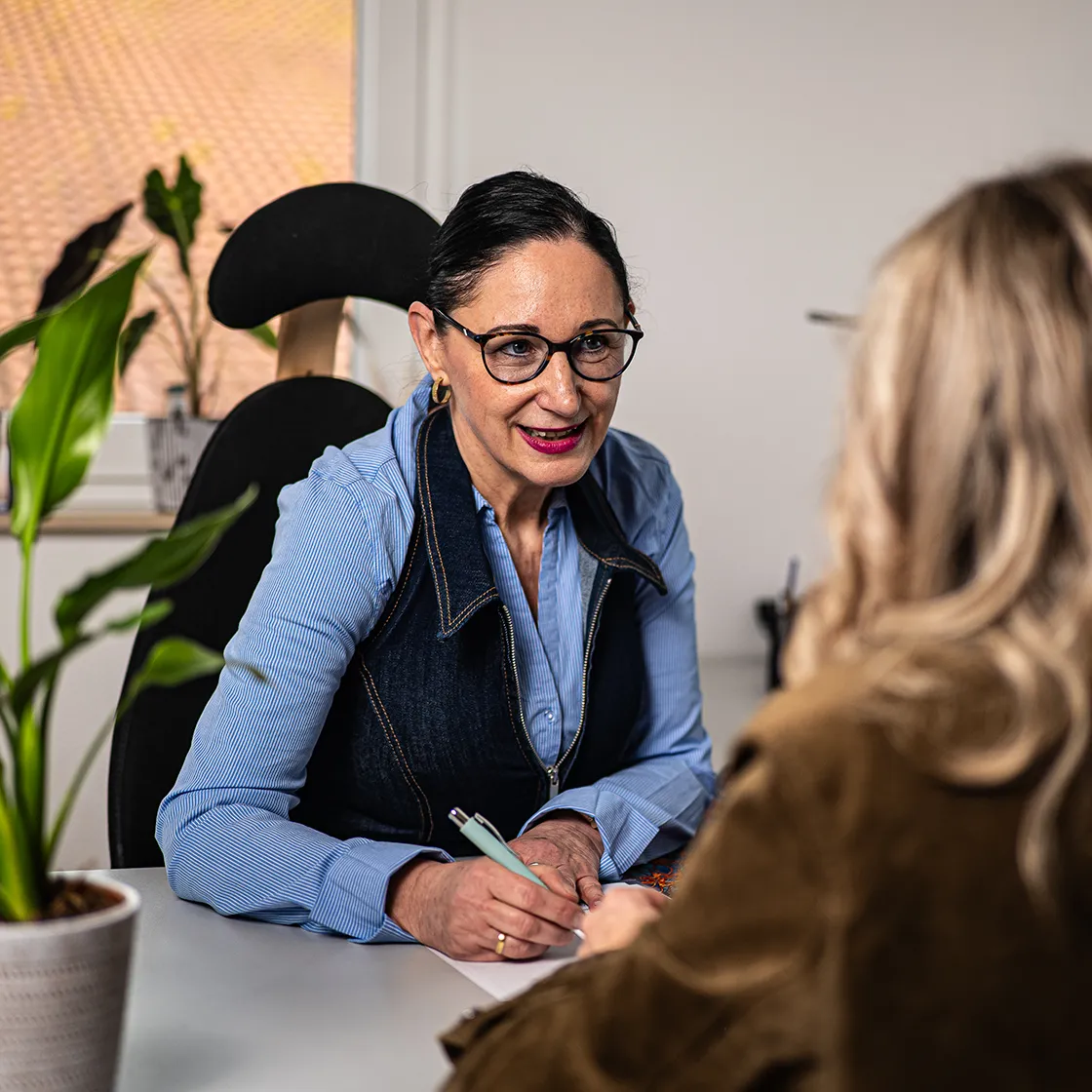 Beratungsgespräch zwischen Mitarbeiterin und Angehöriger am Schreibtisch