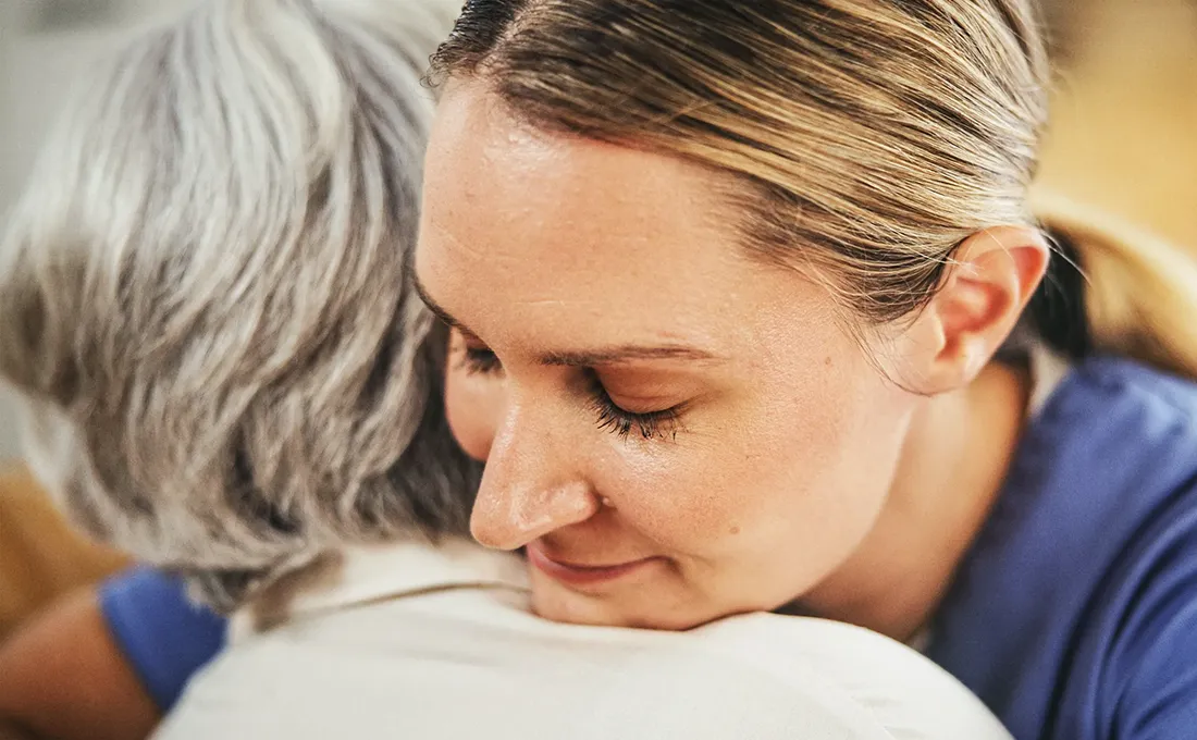 Pflegekraft umarmt Seniorin unterstützend im Alltag