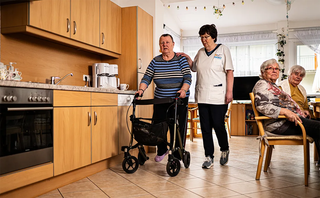 Pflegekraft unterstützt Senior mit Rollator in Wohngemeinschaft