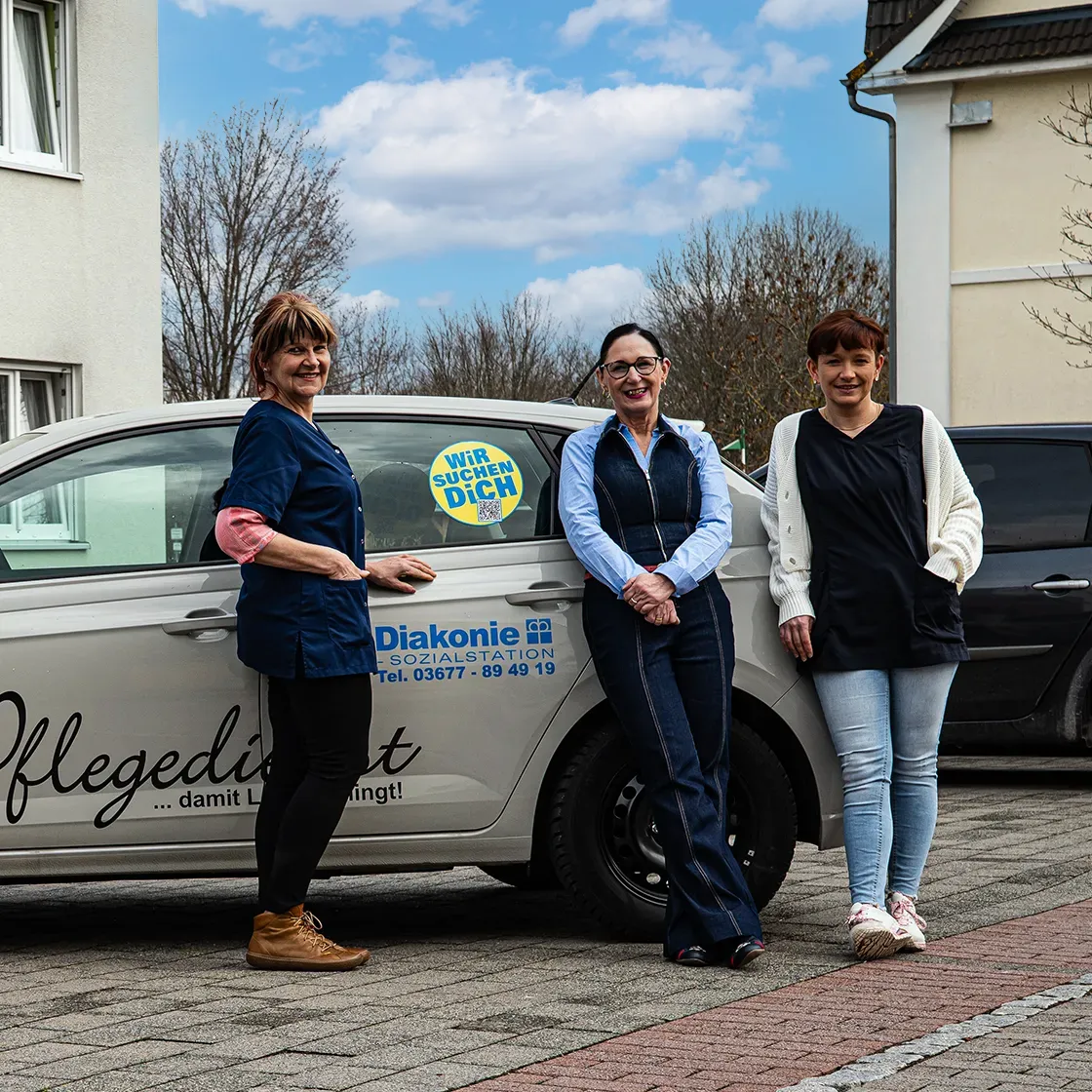 Pflegekräfte der Diakonie Sozialstation Ilmenau stehen vor Dienstfahrzeug im Außenbereich