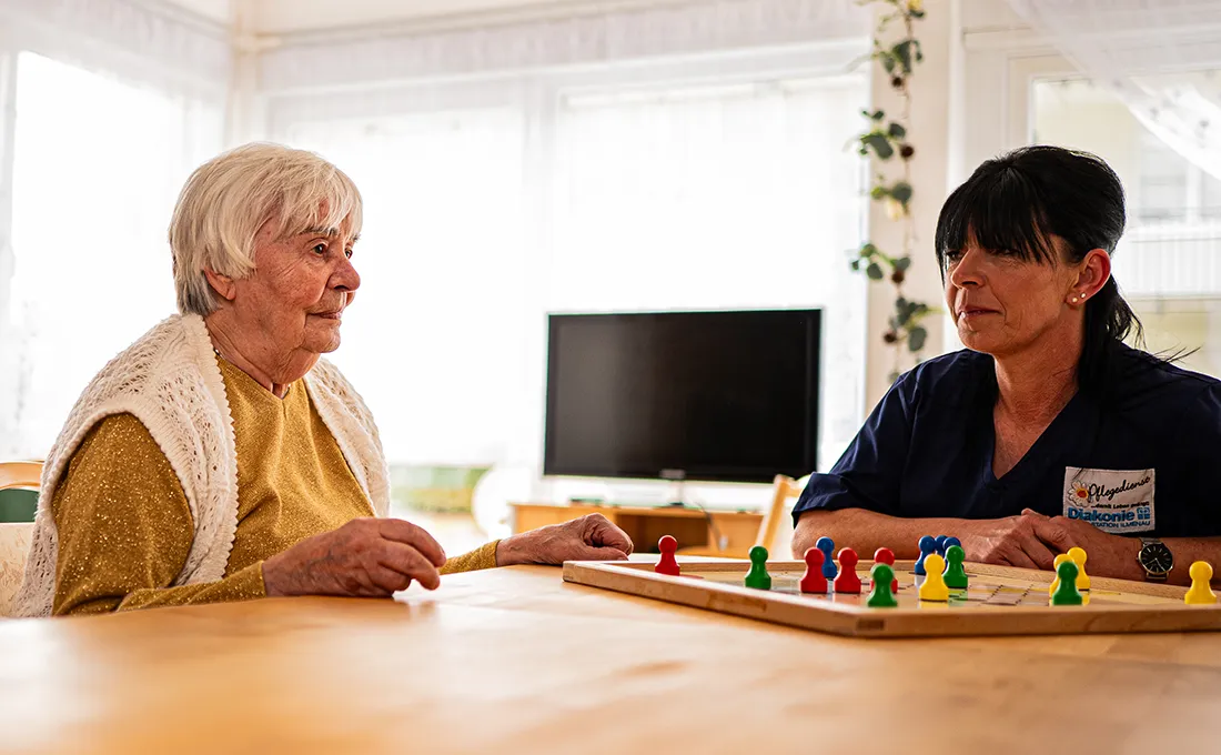 Pflegekraft und Seniorin spielen gemeinsam ein Brettspiel im Alltag