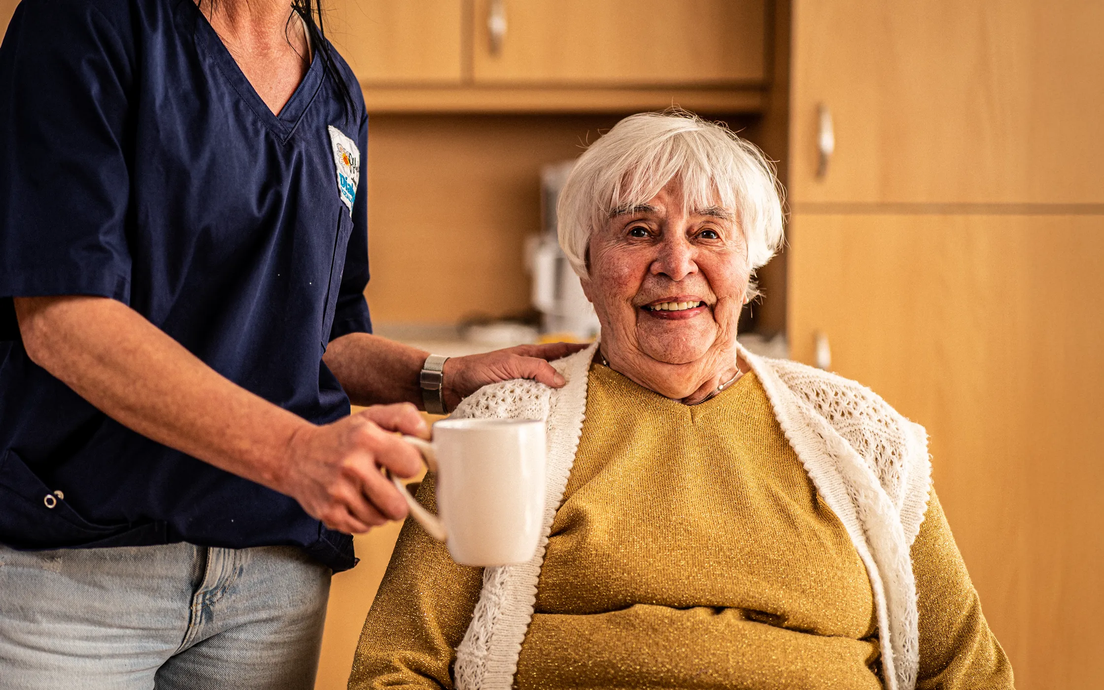 Pflegekraft unterstützt Seniorin im Alltag mit Getränk