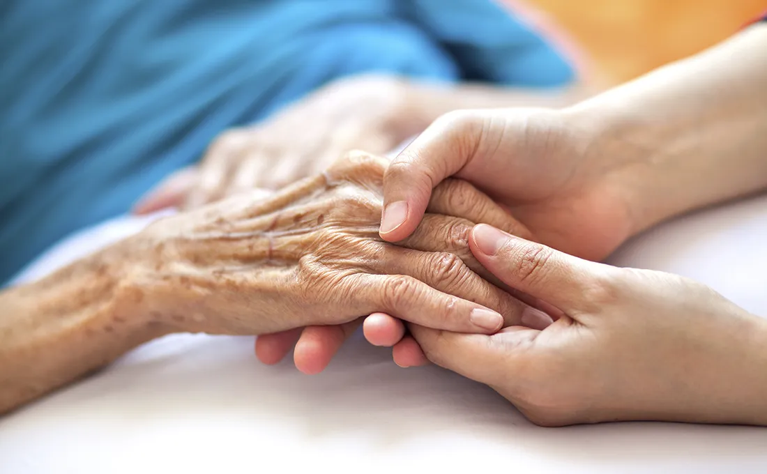 Hände einer Pflegekraft halten unterstützend die Hand einer Seniorin