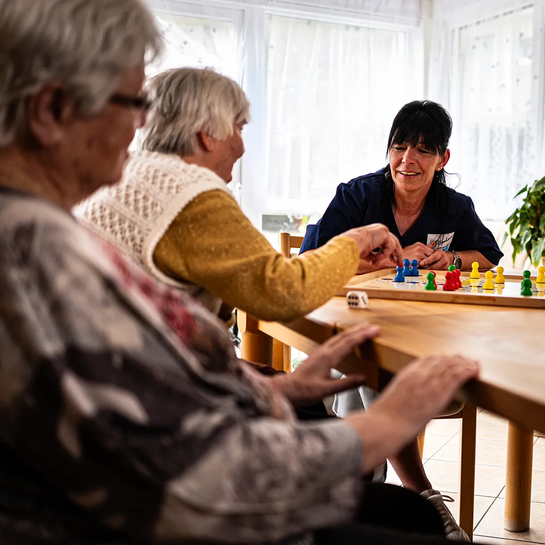 Pflegekraft spielt Gesellschaftsspiel mit Seniorinnen in Wohngemeinschaft